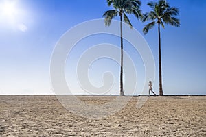 Woman jogging at the beach between two palm trees