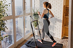 Woman jogging on the modern compact treadmill at her home