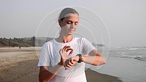 Woman is jogging on the ocean beach and using fitness watch timer.