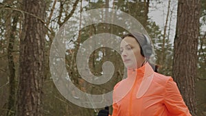 Woman jogging in park. Confident focused female athlete in headphones and orange jacket running in the morning at winter forest. P