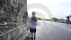 Woman jogging on road near rock cliff