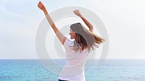 Woman jump with joy at cliff against blue sea on sunny day. Carefree female dancing in slow motion