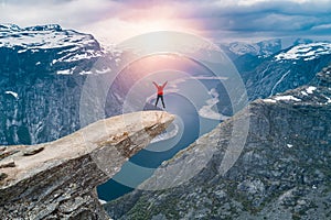 A woman Jump on the mountains cliff edge of Trolltunga throning over Ringedalsvatnet  watching the sunset and snowy