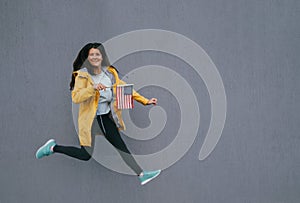 Woman jumping against gray wall outdoor and holding USA flag