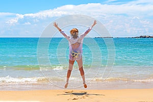 A woman jumping on the beach in front of ocean with feeling happy and freedom