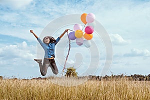 Woman jumping with colorful balloons in the meadow
