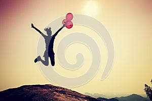 Woman jumping with colorful balloons on sunrise mountain peak