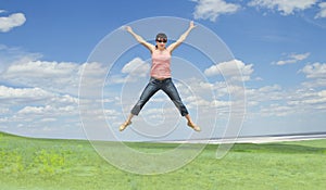 Woman jumping on green grass over blue sky