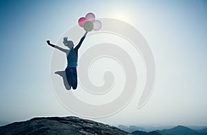 Woman jumping on mountain top with balloons