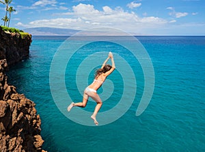 Woman jumping off cliff into the ocean