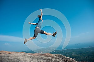 Woman jumping on rocky mountain peak
