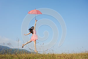 Woman jumping to blue sky with red umbrella