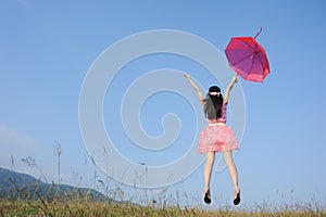 Woman jumping to blue sky with red umbrella