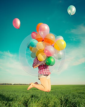 Woman jumping with toy balloons in spring field