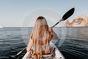 Woman in kayak back view. Happy young woman with long hair floating in kayak on calm sea. Summer holiday vacation and