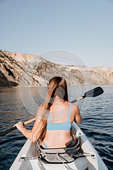 Woman in kayak back view. Happy young woman with long hair floating in kayak on calm sea. Summer holiday vacation and