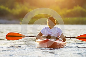 Woman kayaking on river alone with sunset on background