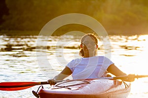 Woman kayaking on river alone with sunset on background