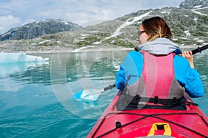 Woman kayaking on Styggvatnet glacier lake near Jostedalsbreen glacier.