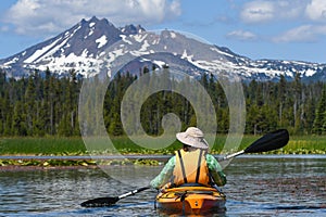 Woman kayaking toward snowy mountain peak