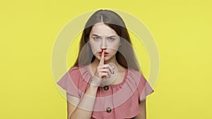 Woman keeping finger near lips, showing silence gesture.