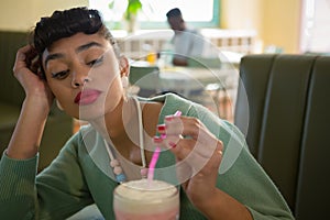 Woman keeping her head on hand while looking at milkshake