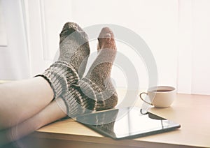 Woman keeping legs in socks on table with tablet