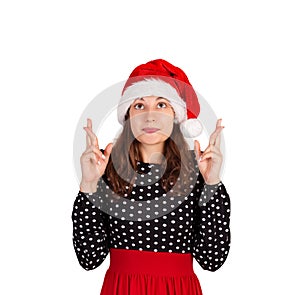 Woman keeps hands raised, fingers crossed and dreams about something. emotional girl in santa claus christmas hat isolated on whit