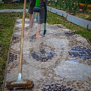 Woman legs washing carpet on grass from hose