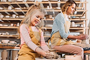 woman and kid making ceramic pots on pottery wheels