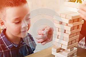 Woman and kid are playing jenga game. Trying to keep balance of tower from wooden blocks. Family leasure time. Concept