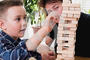 Woman and kid are playing jenga game. Trying to keep balance of tower from wooden blocks. Family leasure time. Concept