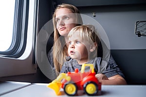 Woman with kid in a train compartment looks out the window. Family travel, holidays