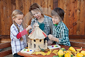 Woman with kids painting the bird house - preparing for winter