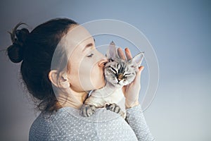 Woman is kissing and cuddling her sweet and cute looking Devon Rex cat. Kitten feels happy to be with its owner. Kitty sits in