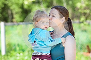 Woman kissing her two year old daughter in her arms, summer park