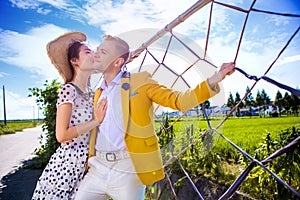 Woman kissing man while standing by fence at field against sky