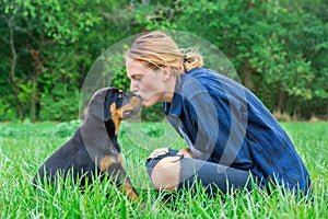 Woman kissing rottweiler puppy in nature