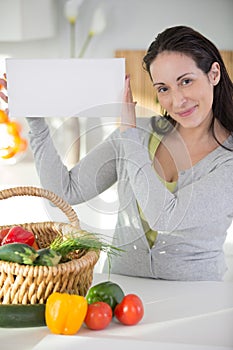 woman in kitchen with basket vegetables holding blank sign