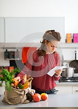Woman in kitchen comparing shopping list to items in bag
