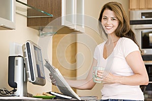 Woman in kitchen at computer with coffee