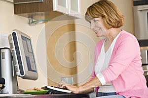 Woman in kitchen with computer and coffee smiling