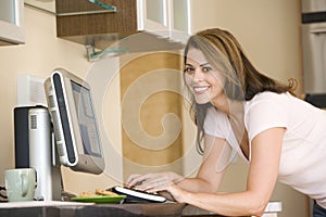 Woman in kitchen with computer smiling