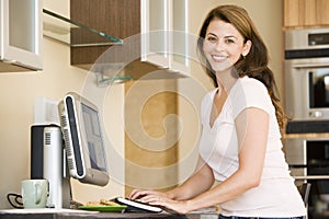 Woman in kitchen with computer smiling