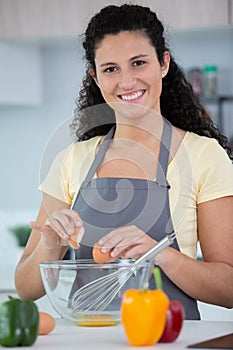 woman in kitchen cracking egg intoa bowl