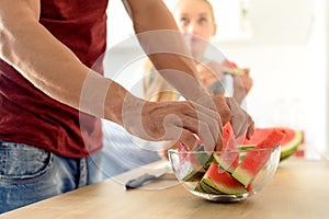 woman in a kitchen eating red watermelon and looking at her husband, Couple in their large contemporary white kitchen