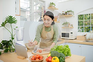 Woman In Kitchen Following Recipe On Digital Tablet