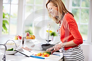 Woman In Kitchen Following Recipe On Digital Tablet