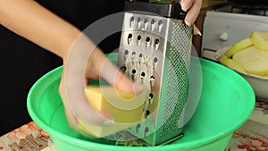 A woman in the kitchen grates hard cheese into a Cup.