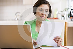 Woman in kitchen with laptop and paperwork